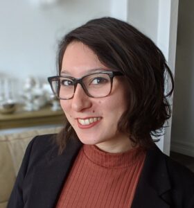 A portrait of Dr. Thornburg, who is smiling. She is wearing eyeglasses and a red blouse under a black jacket. She has chin-length dark hair.